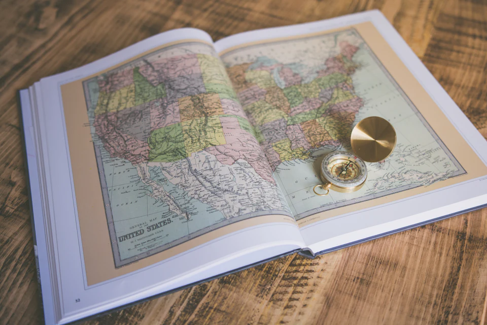 Libro di mappe aperto con una bussola su un tavolo di legno, per pianificare un viaggio