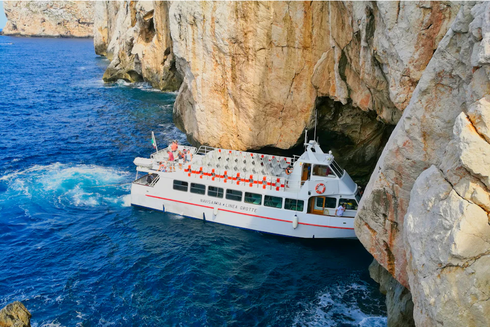 Battello turistico bianco che naviga in acque blu tra alte scogliere calcaree