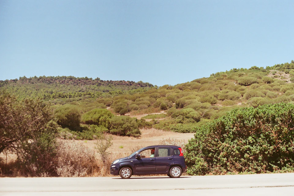 Piccola auto parcheggiata a bordo strada tra colline e macchia mediterranea in Sardegna