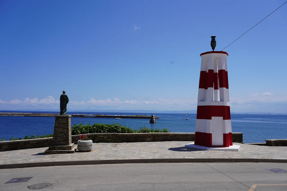 Faro a strisce rosse e bianche e statua sul molo di Stintino con vista sul mare